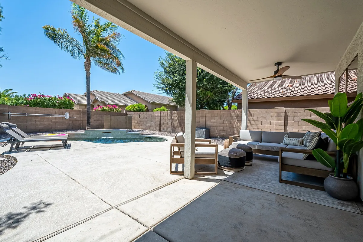 A serene backyard oasis featuring a sparkling swimming pool surrounded by palm trees, neatly landscaped greenery, and an inviting outdoor seating area. The tranquil atmosphere is perfect for both relaxing and entertaining.