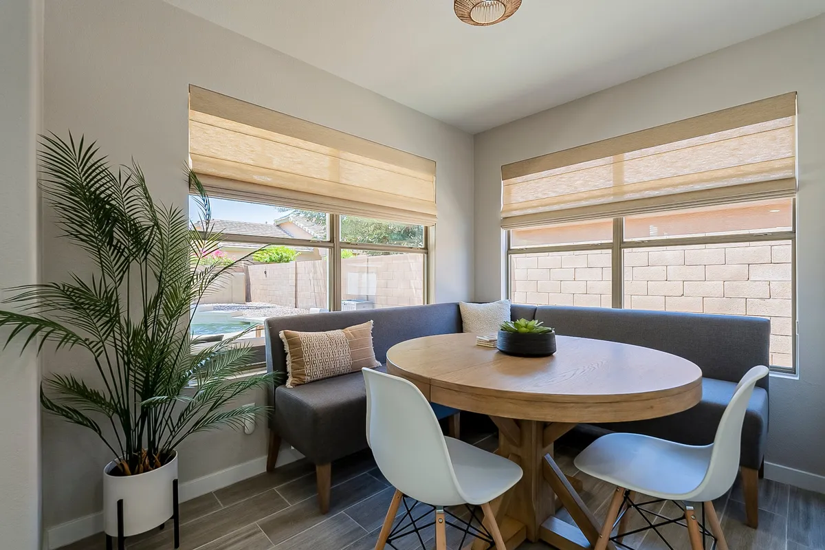 A round wooden dining table is bathed in natural light, surrounded by comfortable chairs and accented by an indoor plant. The scene evokes warmth and intimacy, ideal for casual family meals or friendly brunches.