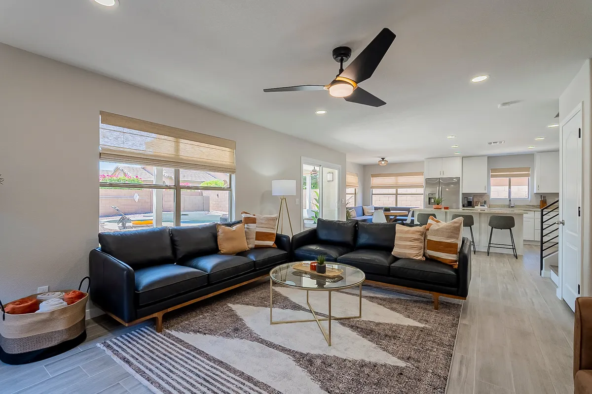 A contemporary living area featuring a black sectional sofa, a glass coffee table, a decorative rug, and expansive windows that let sunlight pour in. The room feels both cozy and upscale, ideal for hosting guests or enjoying quiet moments.