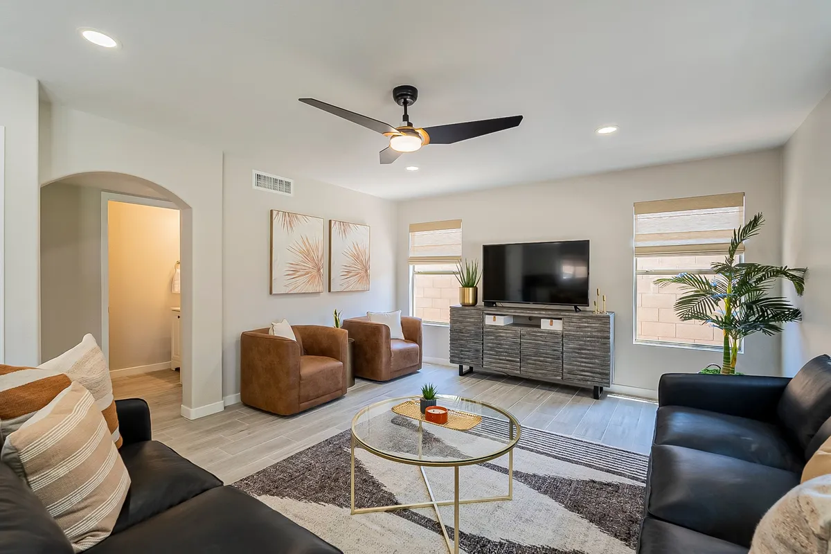 A professionally decorated living room with a plush sofa, stylish armchairs, a glass coffee table, wall-mounted TV, and modern artwork. The space is open, filled with natural light, and designed for both relaxation and social gatherings.
