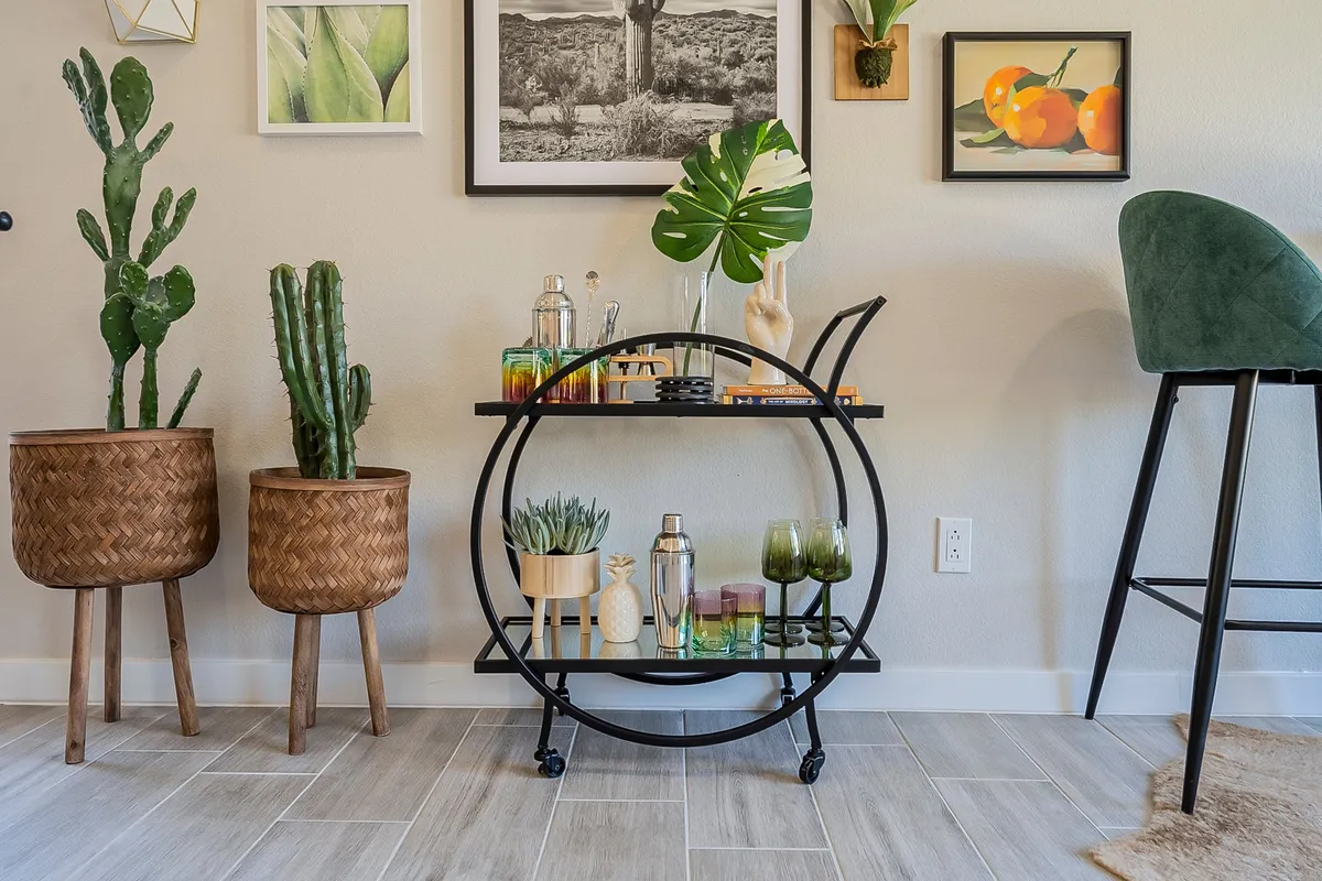 A chic interior bar cart adorned with glassware, greenery, cacti, and framed artwork, ready for mixing drinks. The setup exudes a stylish, playful vibe and suggests opportunities for hosting cocktail hours or casual celebrations inside.
