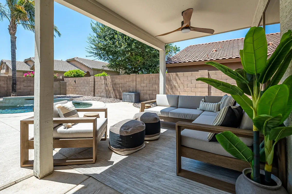 A welcoming patio area with comfortable outdoor seating, a sparkling swimming pool, and lush potted plants. The space is designed for relaxation and entertaining, surrounded by greenery that enhances the retreat-like feel.