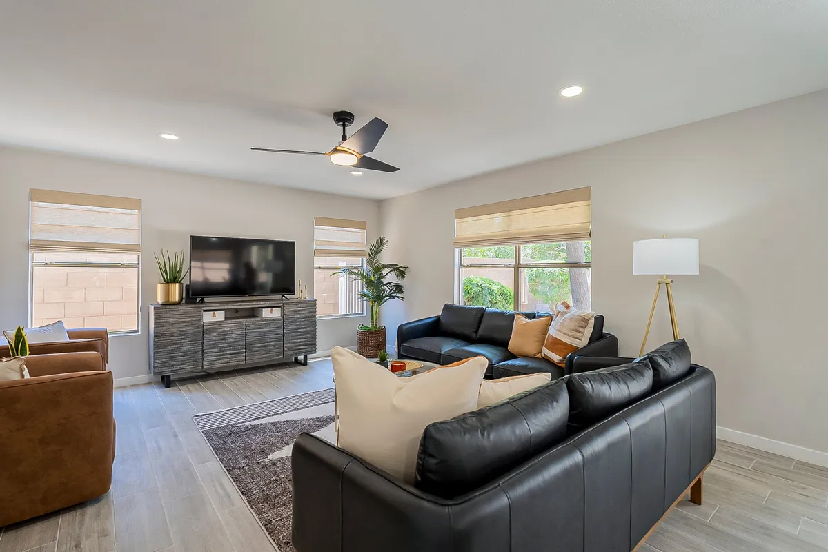 A comfortable living room with a plush sofa, television, leafy plants, a statement light fixture, and a textured rug underfoot. The overall look is cozy and welcoming, designed for both socializing and relaxation.