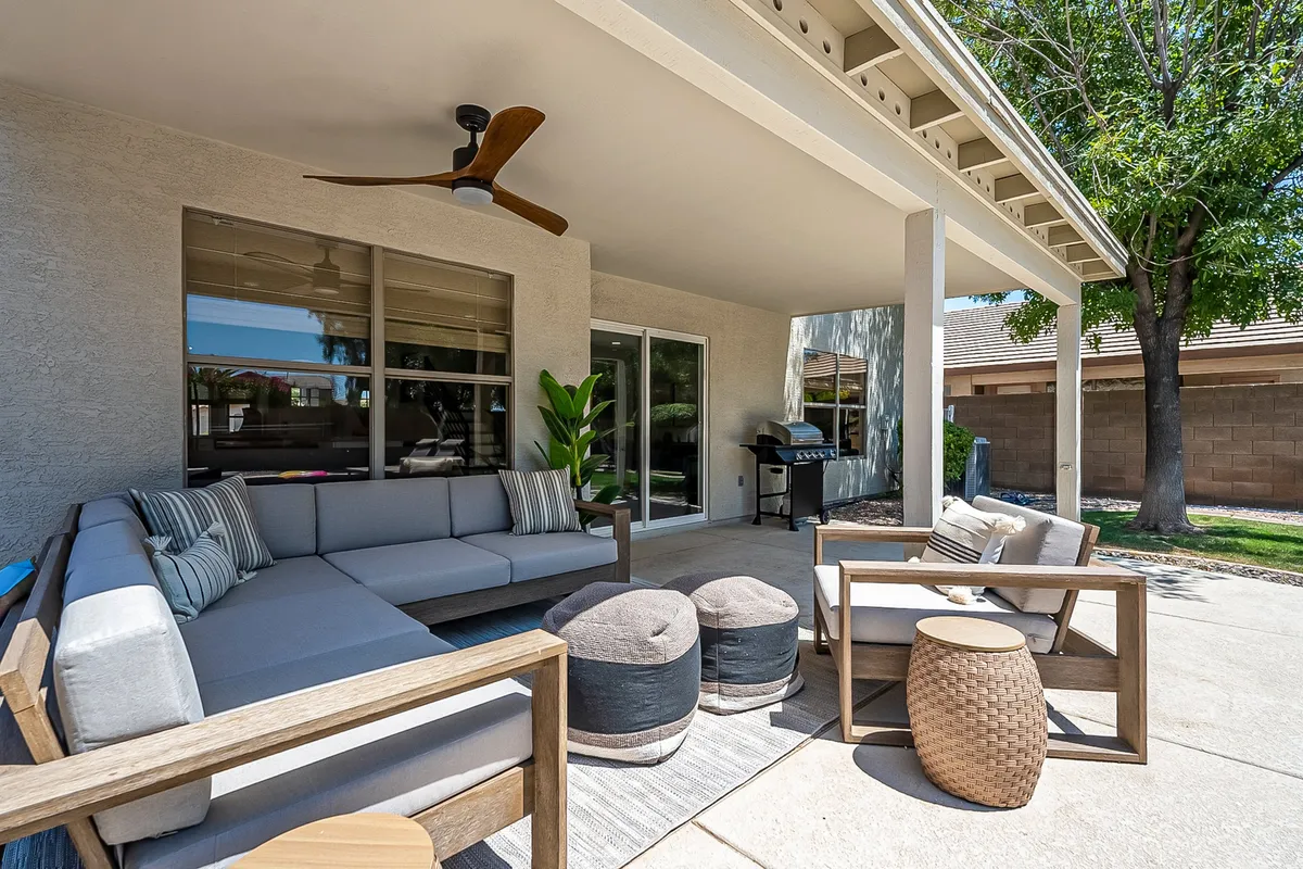 A contemporary outdoor area featuring a large sectional sofa and coffee table surrounded by green plants, with a grill in the background. The space is set up for al fresco entertaining, providing a comfortable spot for friends to gather, share drinks, and enjoy outdoor meals.
